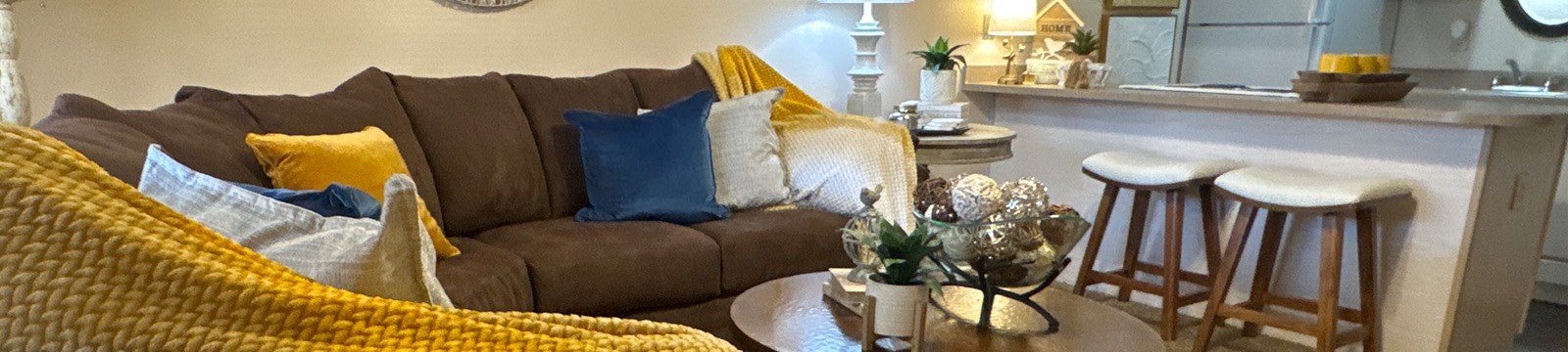 A brown couch with blue and yellow pillows and a yellow throw blanket.
